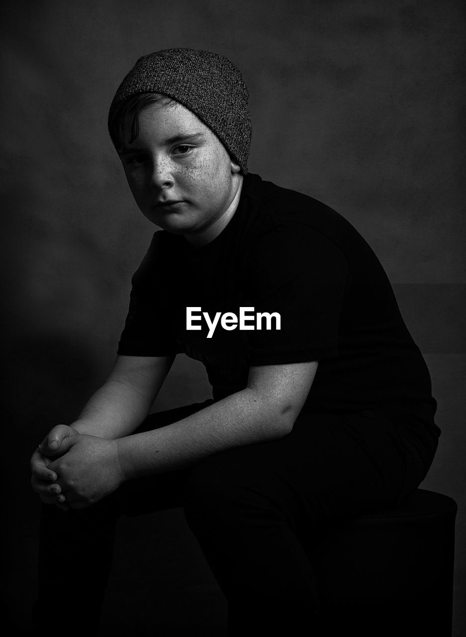 Portrait of teenage boy sitting against sky at dusk