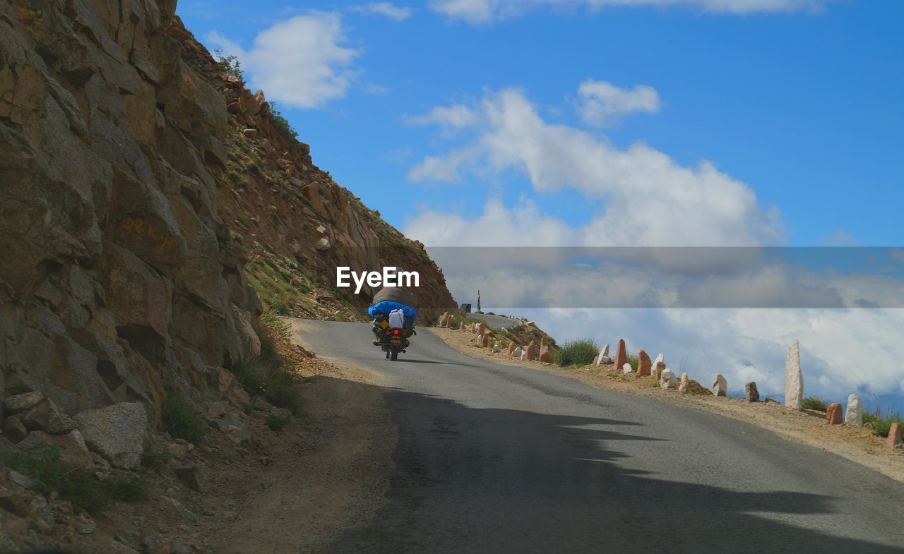 WOMAN RIDING BICYCLE ON ROAD AGAINST SKY