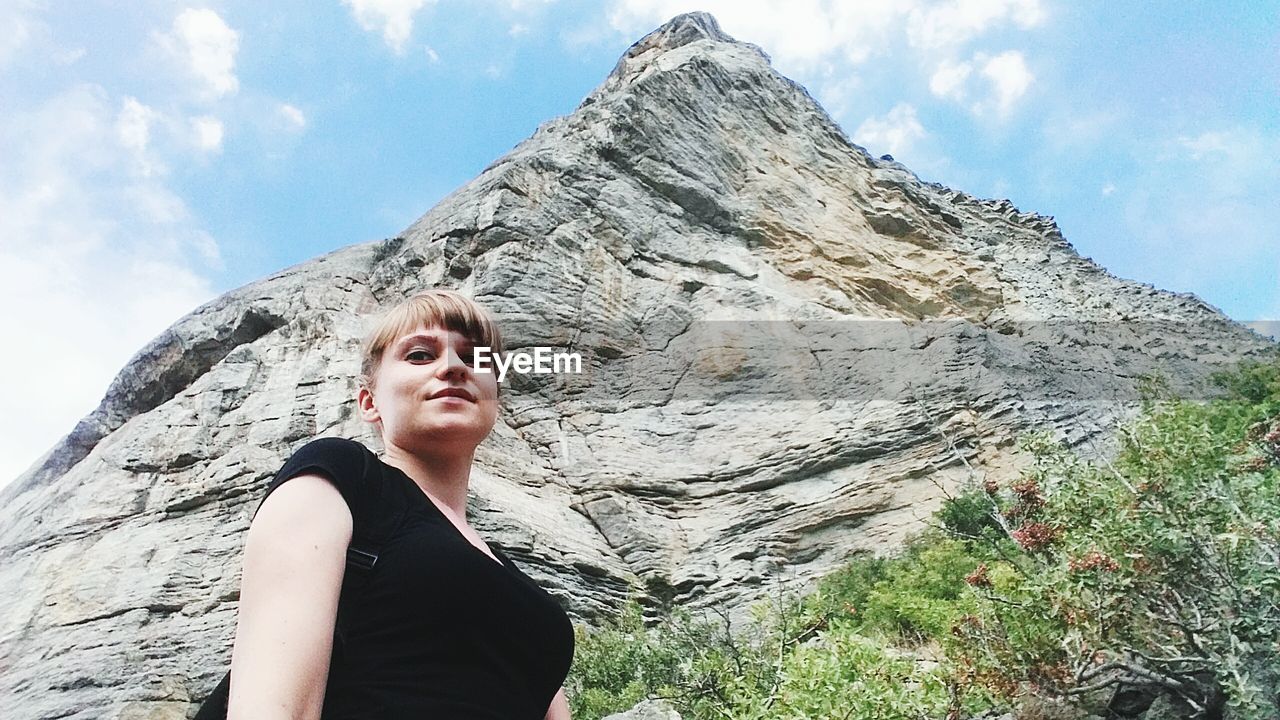 Low angle portrait of young woman standing against cliff