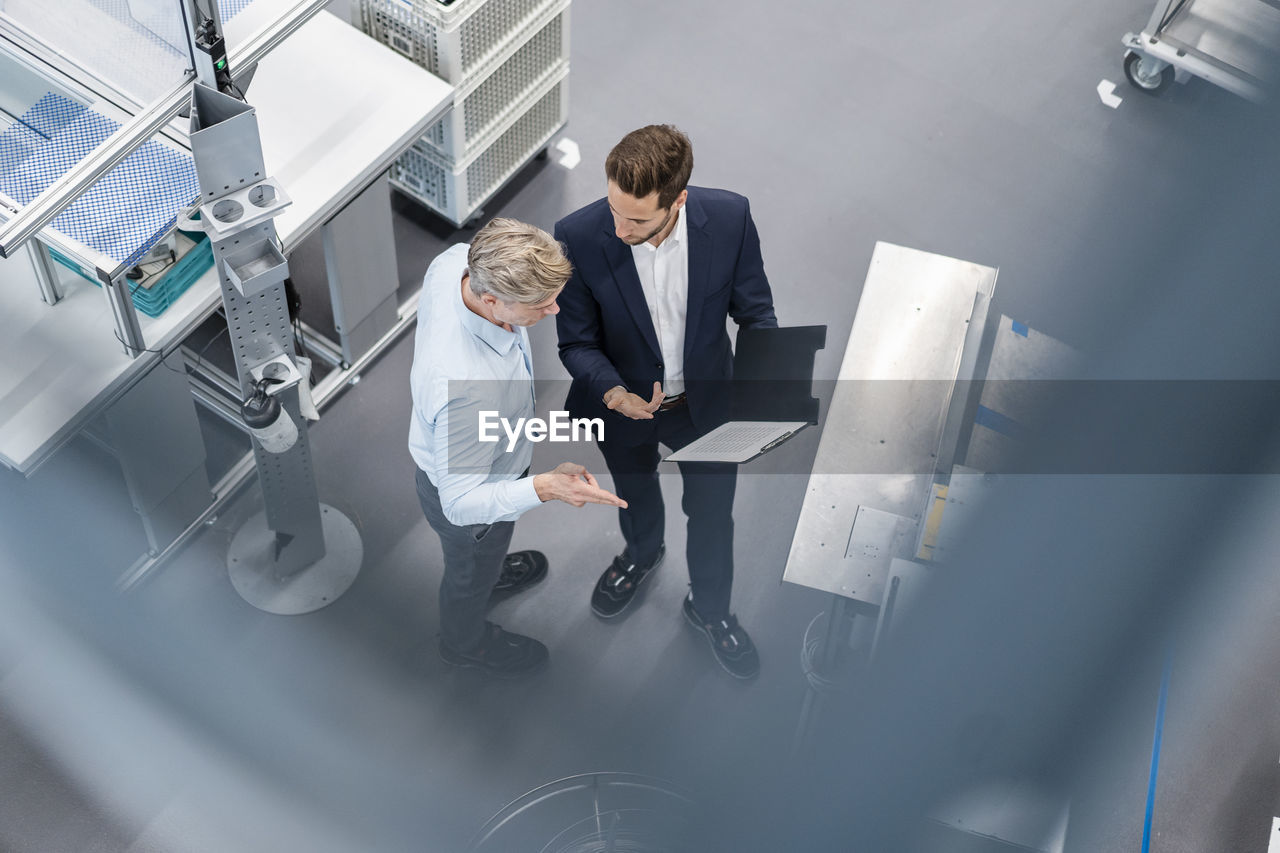 Two businessmen with clipboard talking in a factory