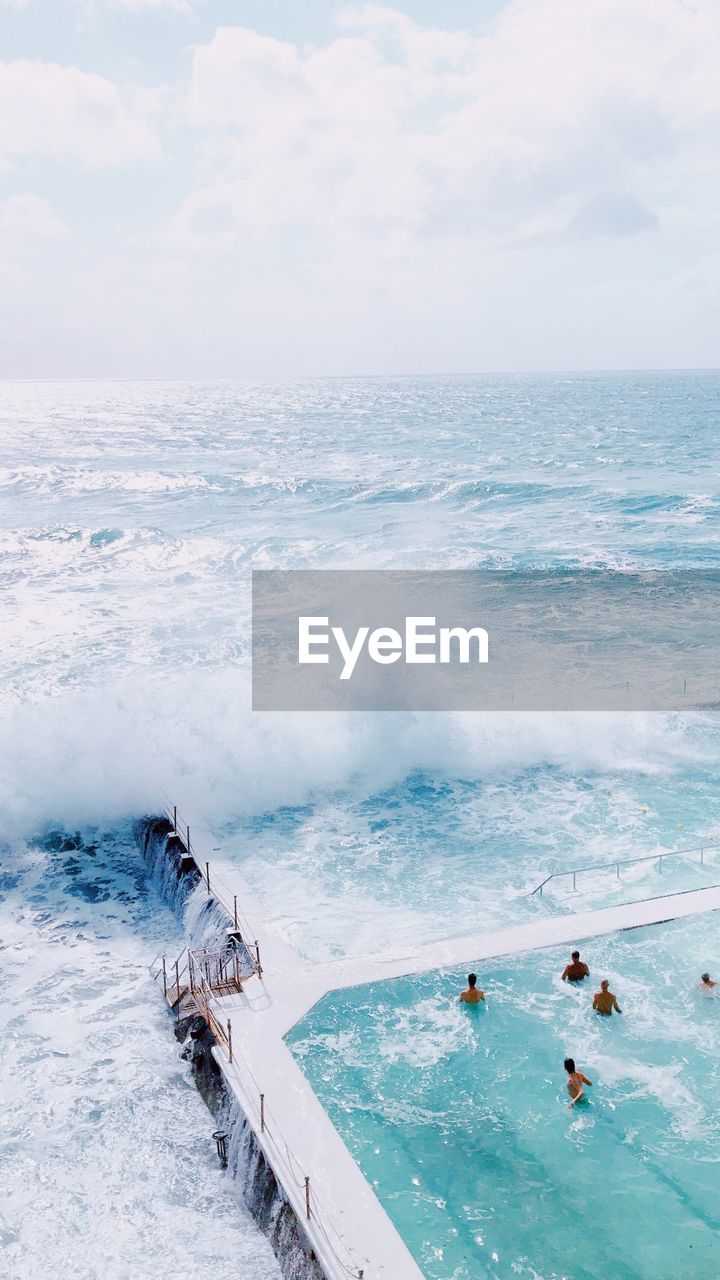 Aerial view of people enjoying in swimming pool by sea