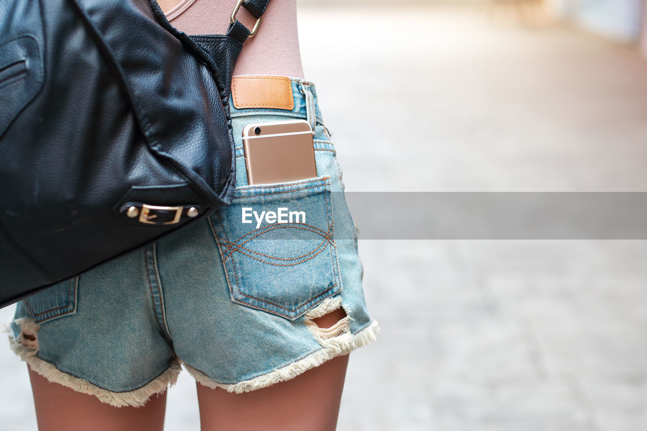 Midsection of woman with bag and phone in pocket standing on land