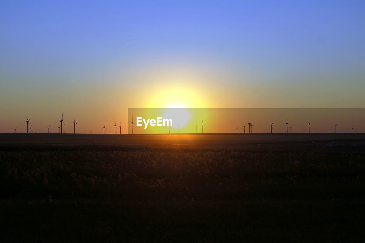 SILHOUETTE OF WIND TURBINES ON FIELD DURING SUNSET