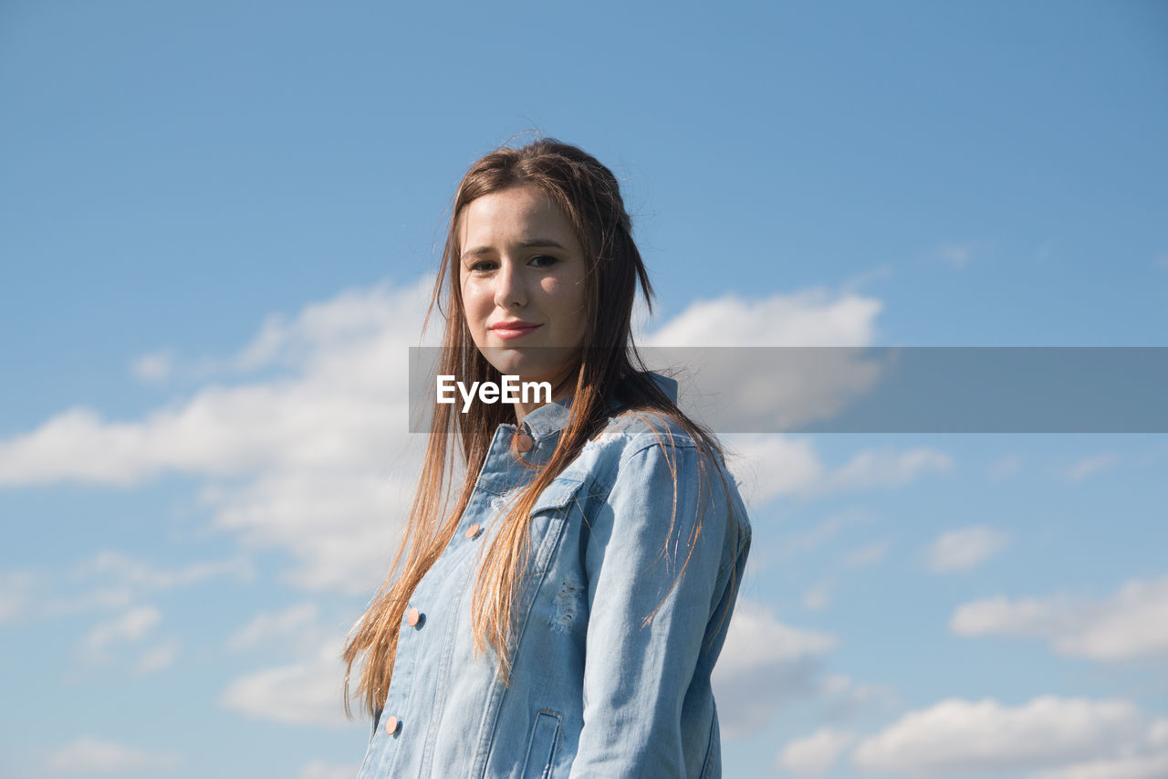 Portrait of young beautiful woman standing against sky