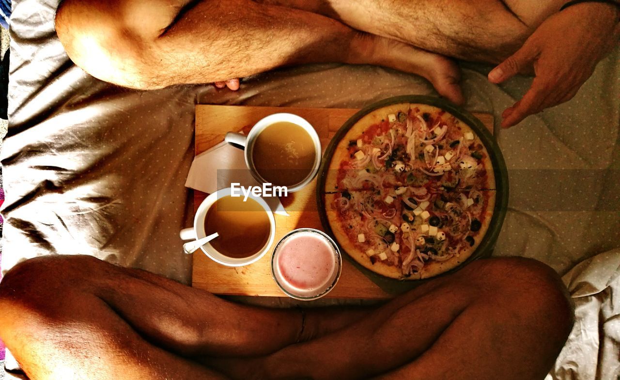 Low section of friends having pizza with coffee on bed