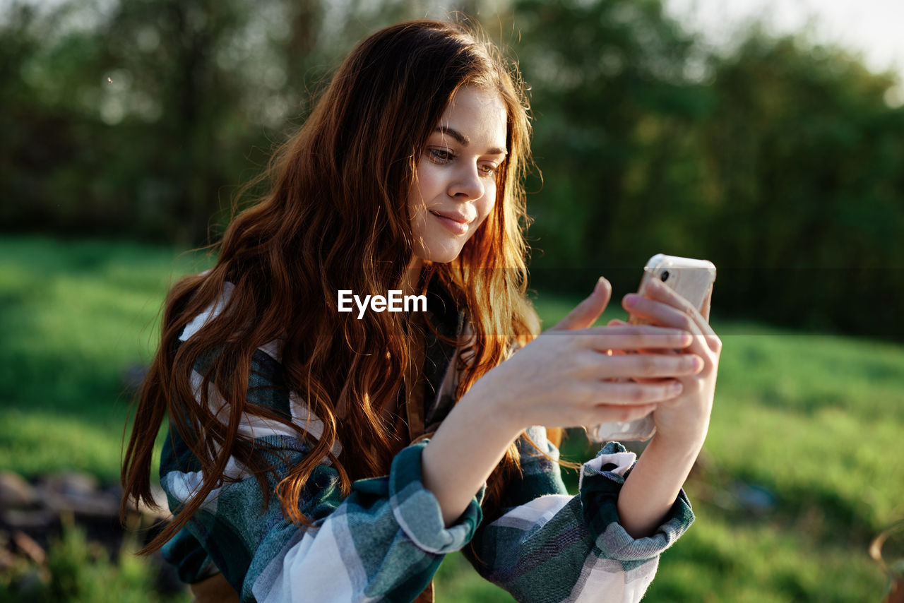 young woman using mobile phone while sitting on field