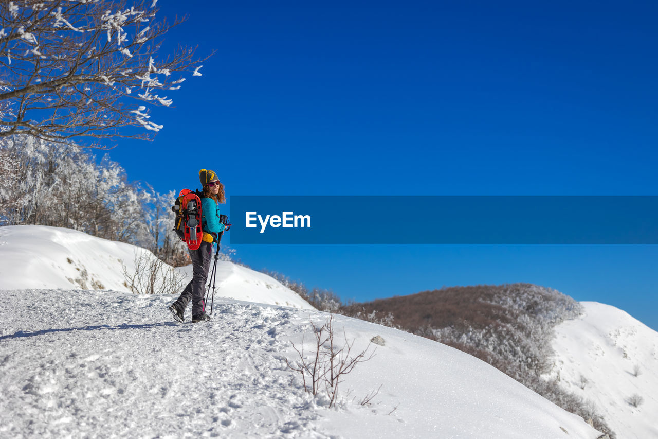 Snow hiker in the mountains, with snowshoes and ski poles, backpack and hat. 