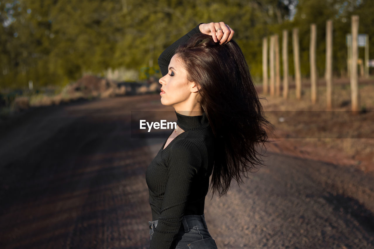 Side view of young woman with hand in hair standing on road