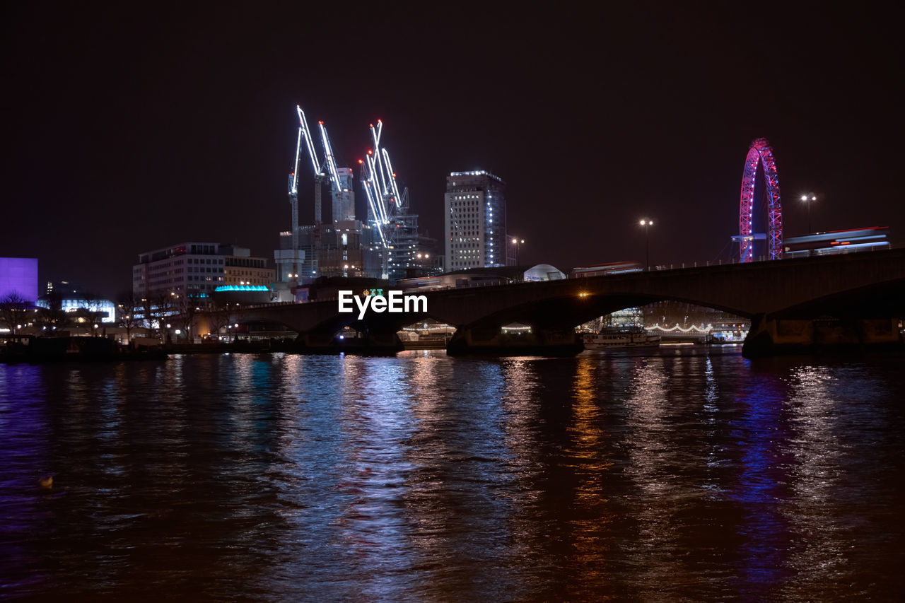 ILLUMINATED BRIDGE OVER RIVER WITH CITY IN BACKGROUND