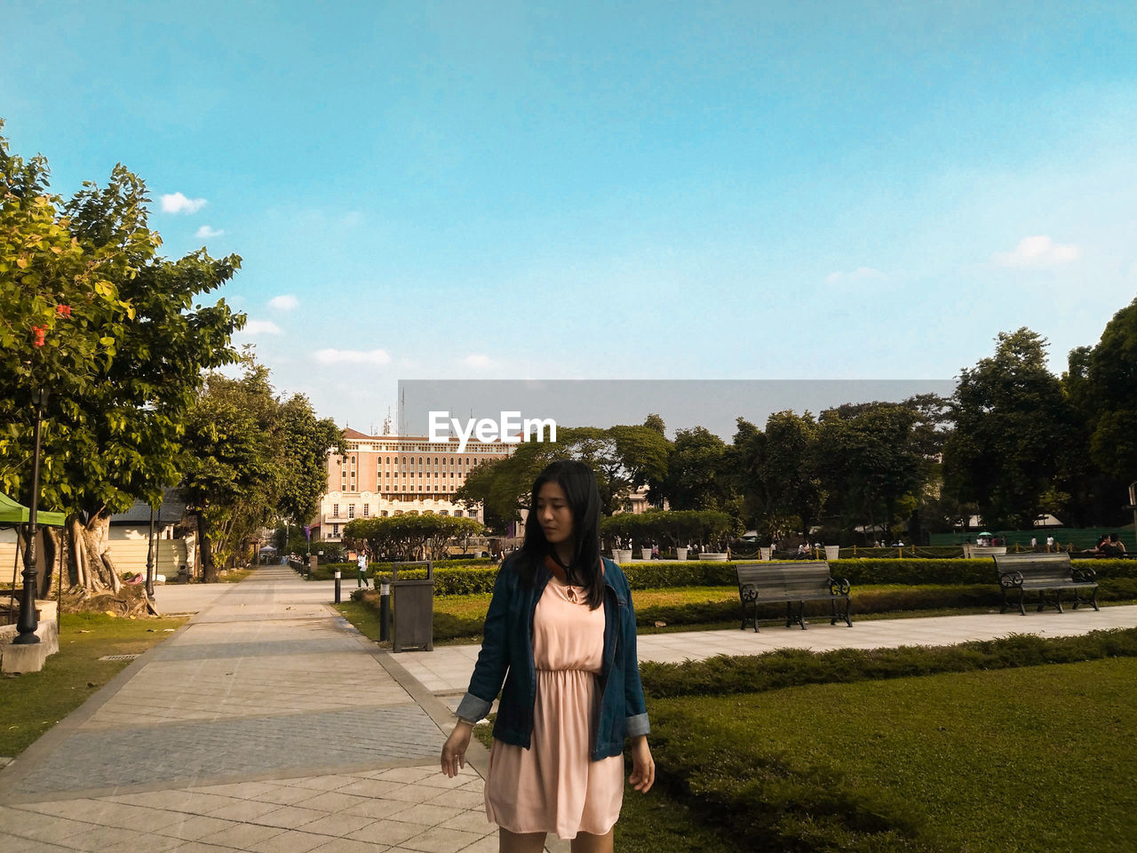 Young woman looking away while standing in park against blue sky