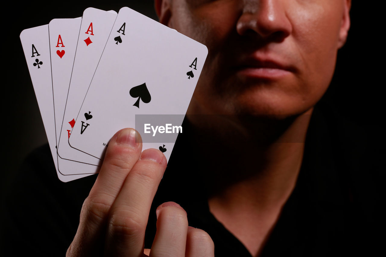 Midsection of man holding aces over black background