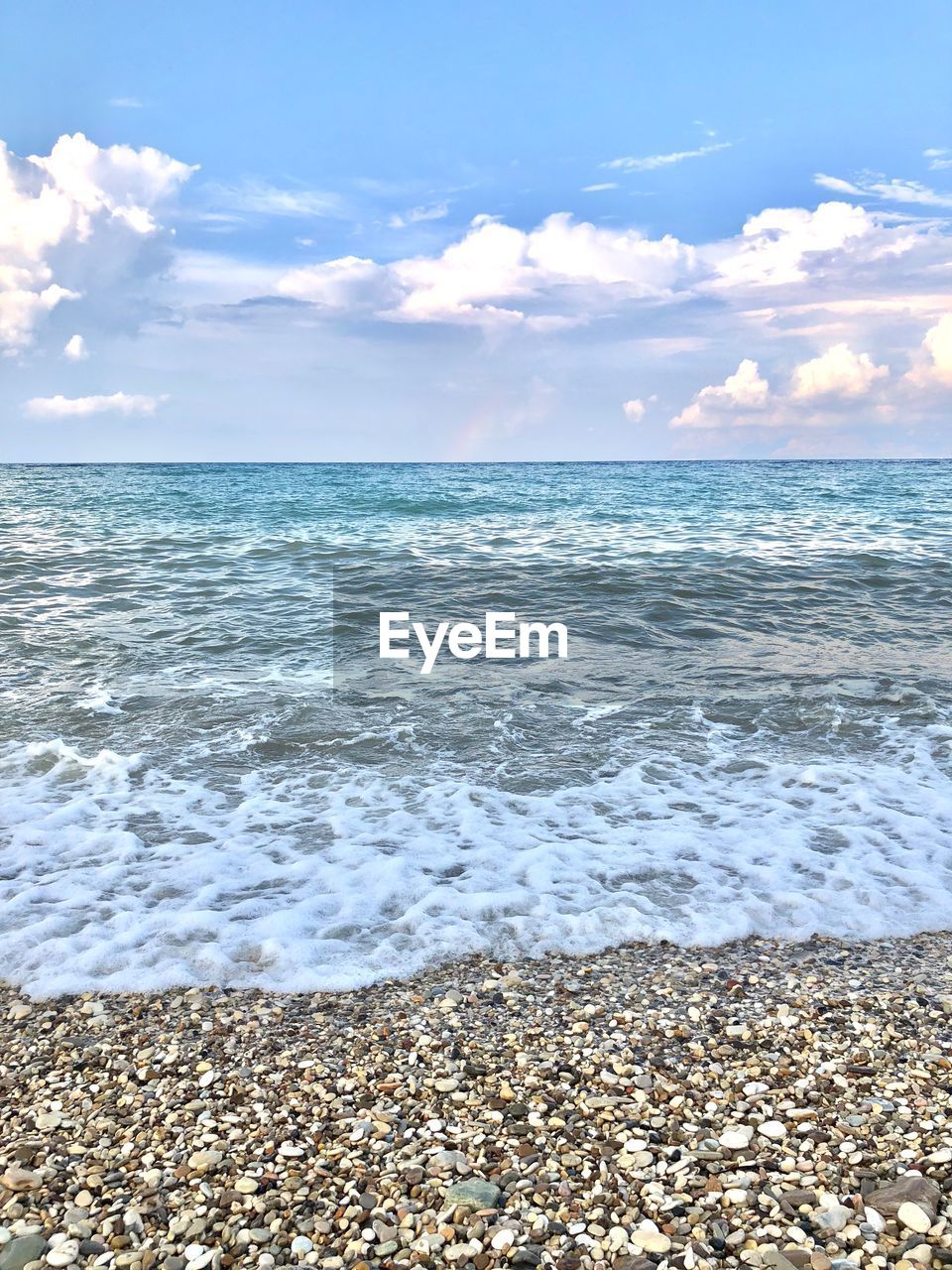 Scenic view of sea by stones at beach against cloudy sky