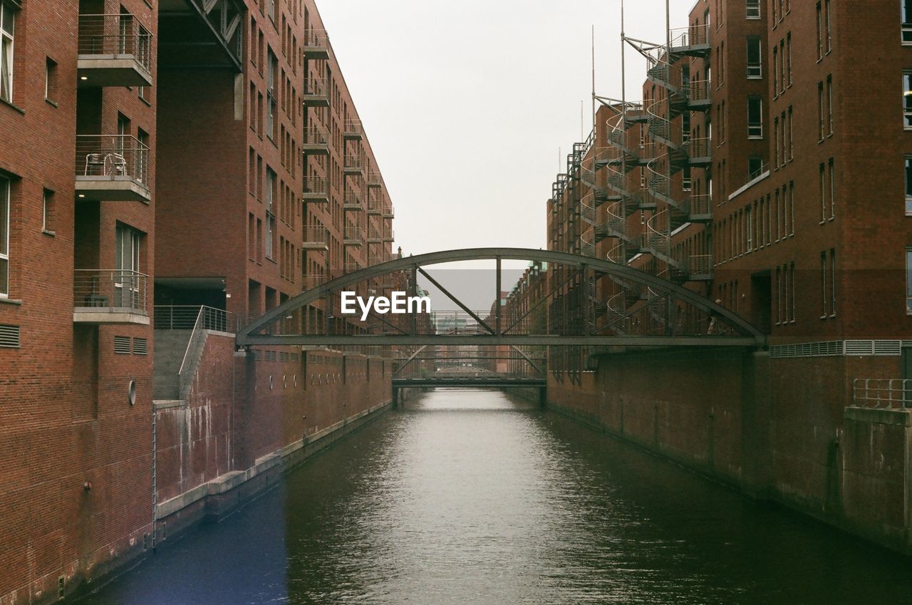 Bridge over canal amidst buildings against sky in city