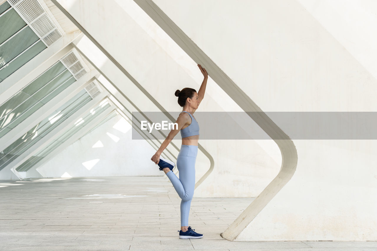 Sporty woman doing a leg stretch, warm up exercise. modern urban background.