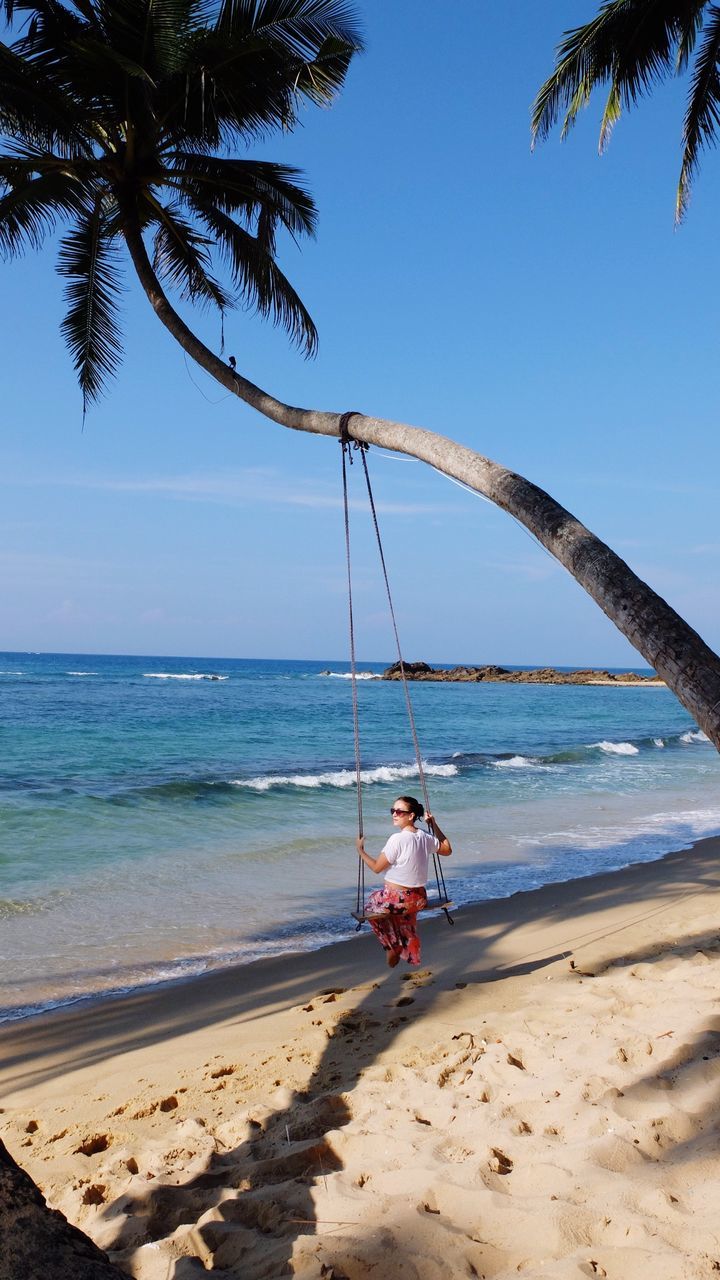 Woman swinging on rope swing at beach against sky