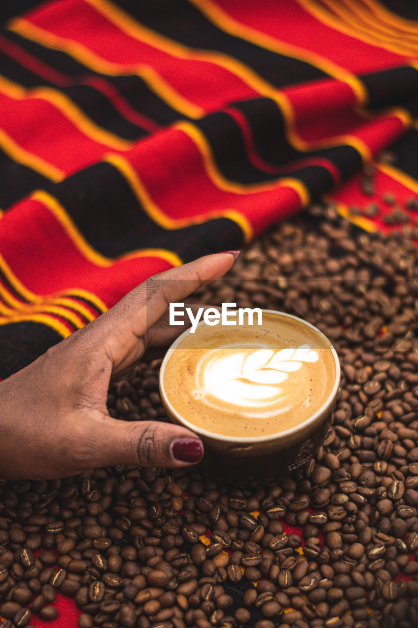 Cappuccino in a ceramic cup with flower or leaves on the foam and roasted coffee beans