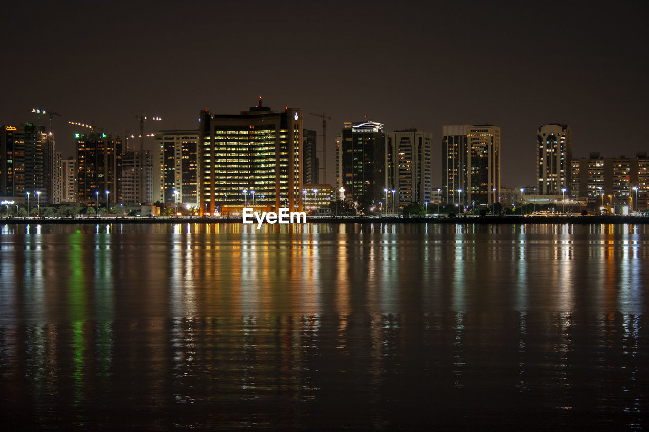 Illuminated buildings by river against sky at night in abu dhabi, united arab emirates