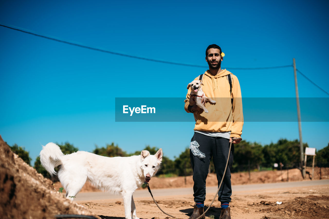 WOMAN WITH DOG STANDING ON FIELD AGAINST SKY