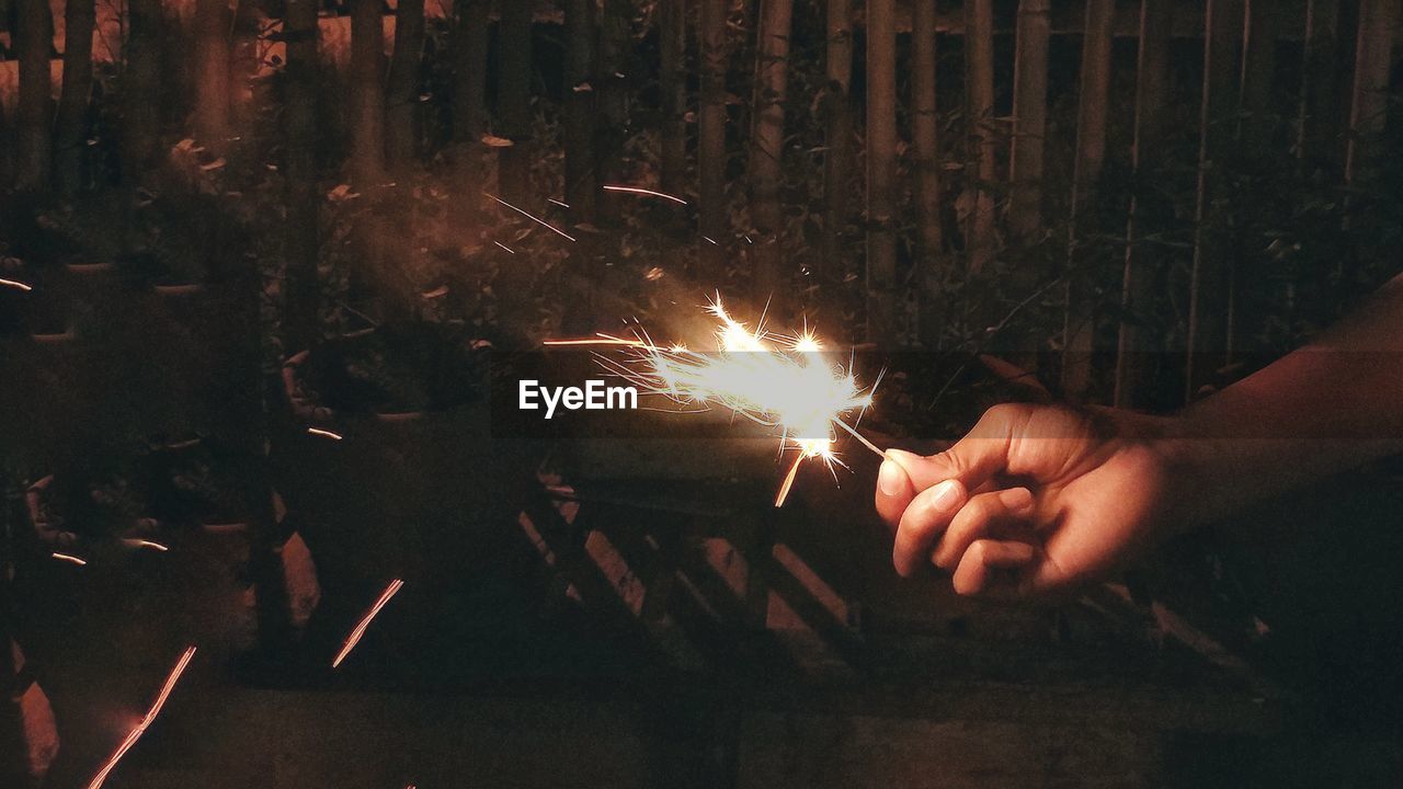 Cropped hand of person holding sparkler at night