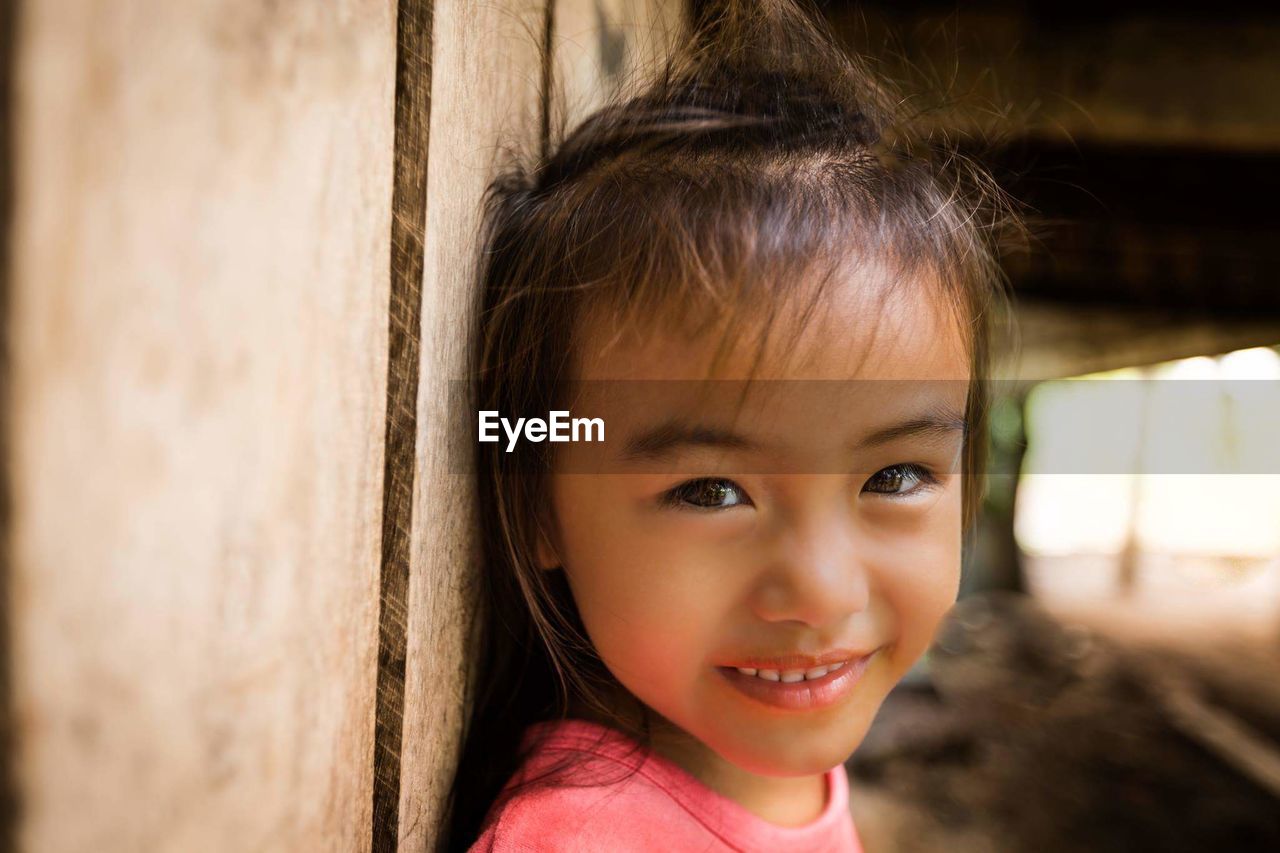 Close-up portrait of girl standing by wooden fence