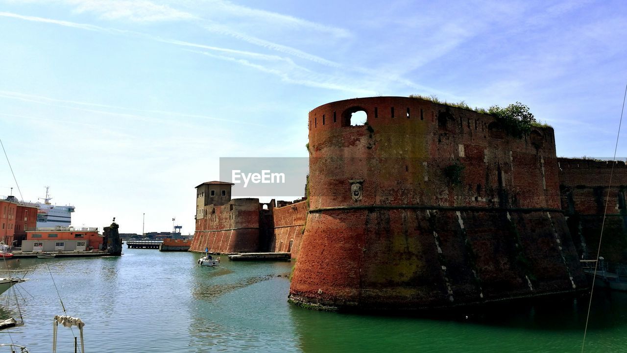 OLD RUSTY BUILDING BY RIVER AGAINST SKY