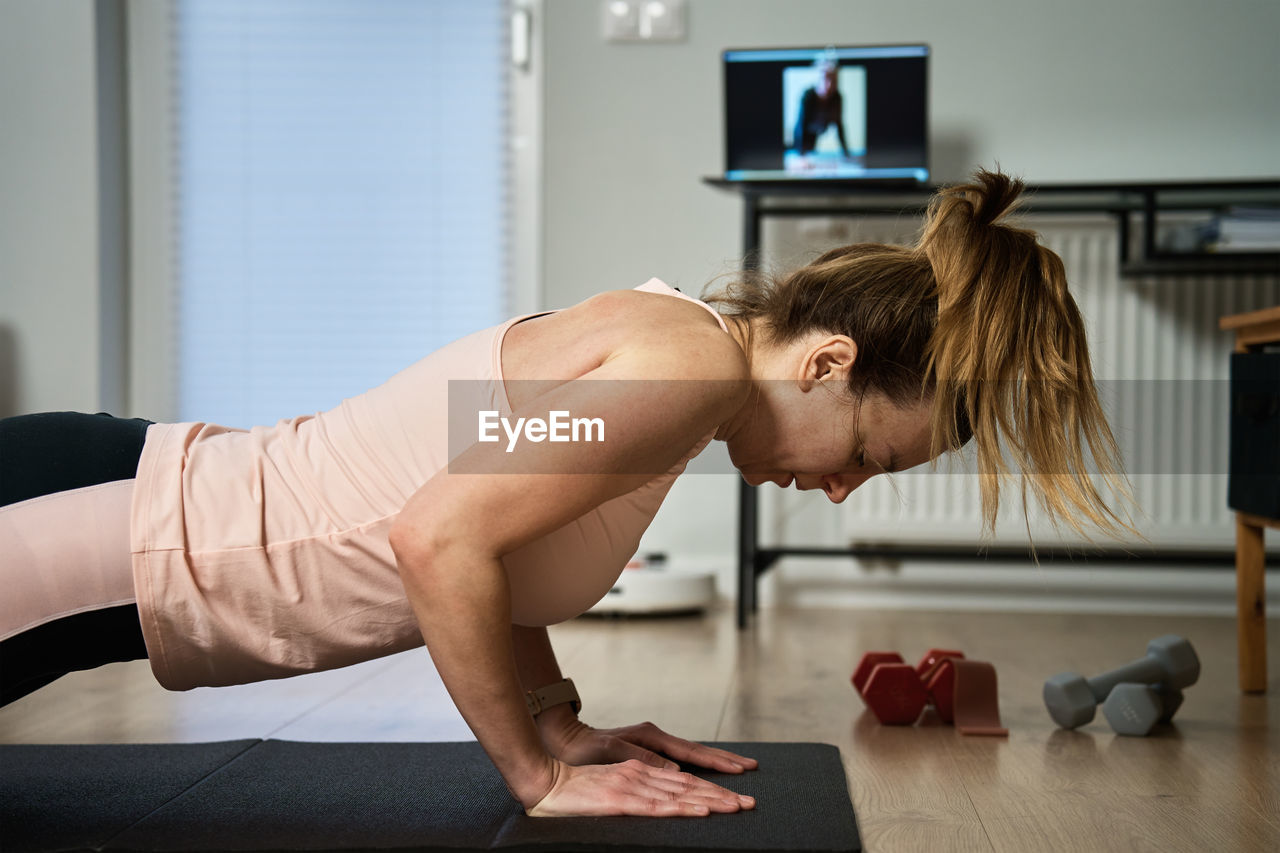 Woman in sports clothes does fitness cardio exercises at home, using laptop