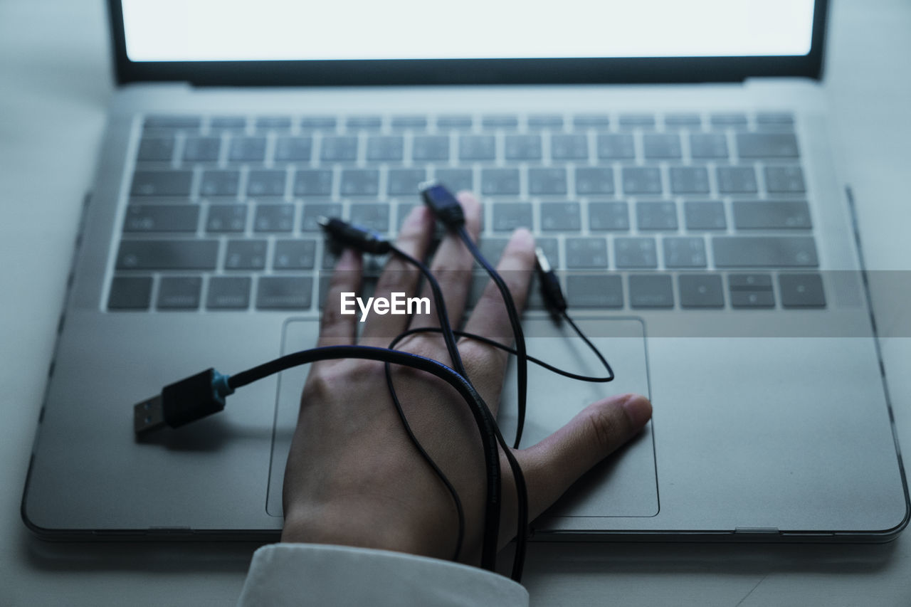 Cropped image of hand with cables on laptop