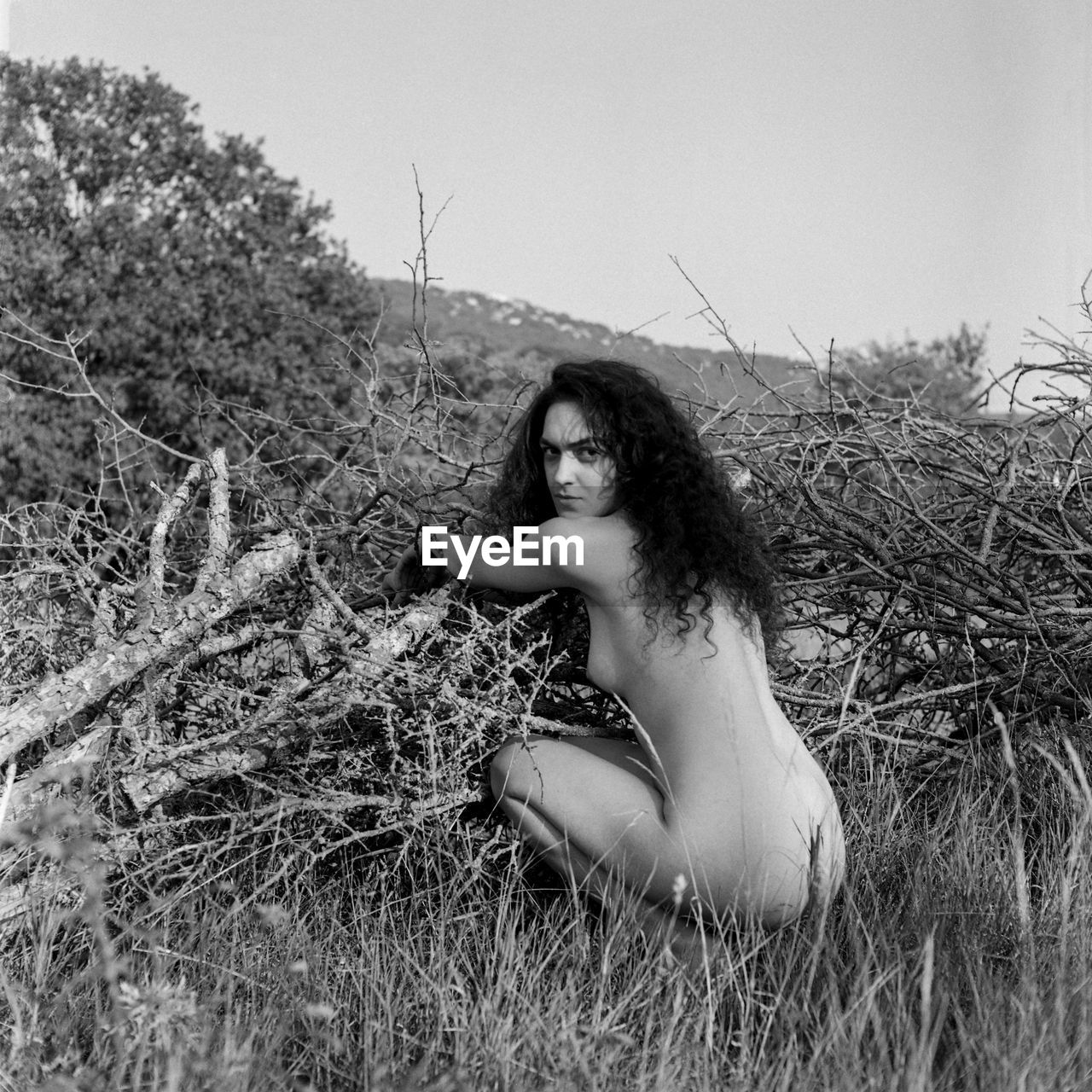 Portrait of naked woman crouching on field