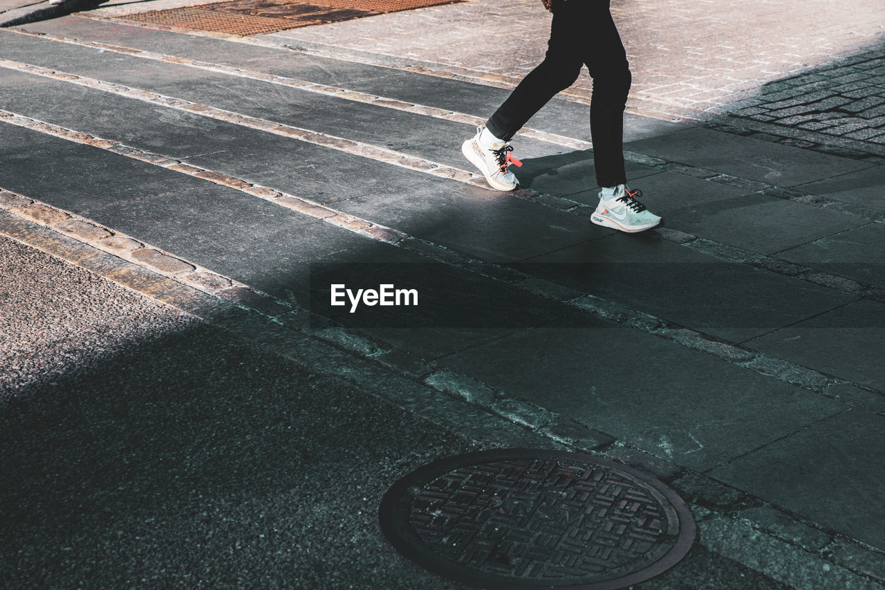 LOW SECTION OF WOMAN STANDING ON COBBLESTONE STREET