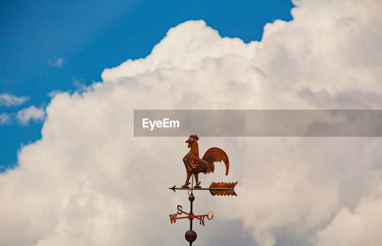 Weather vane against cloudy sky