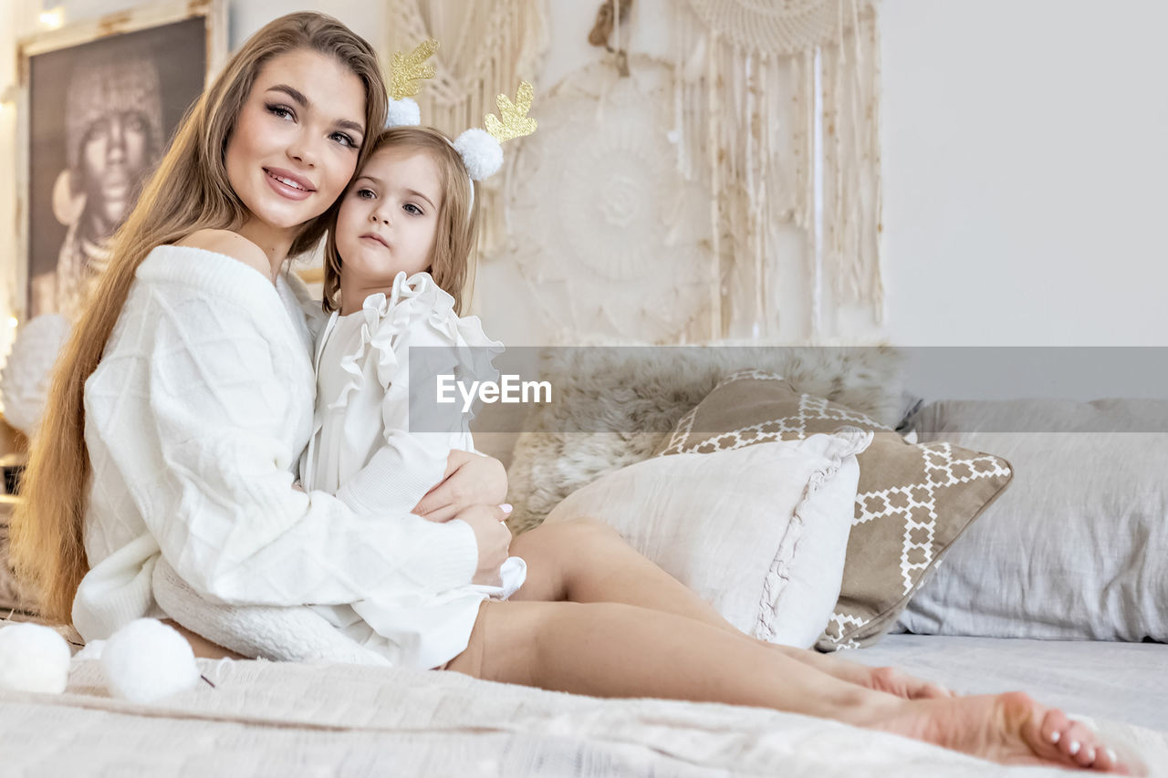 Mom and daughter hug each other, sitting on the bed in a bright bedroom.family. ethno-interior 