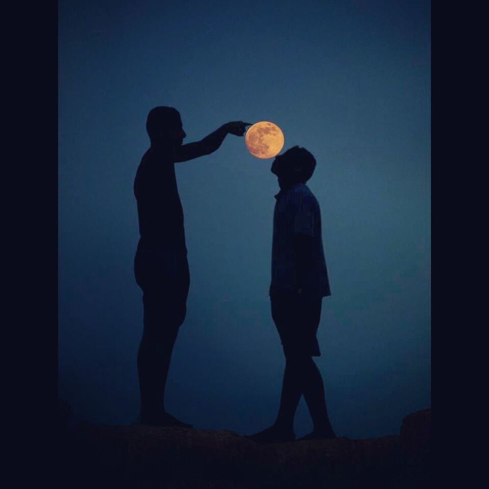 Optical illusion of silhouette men touching full moon at night