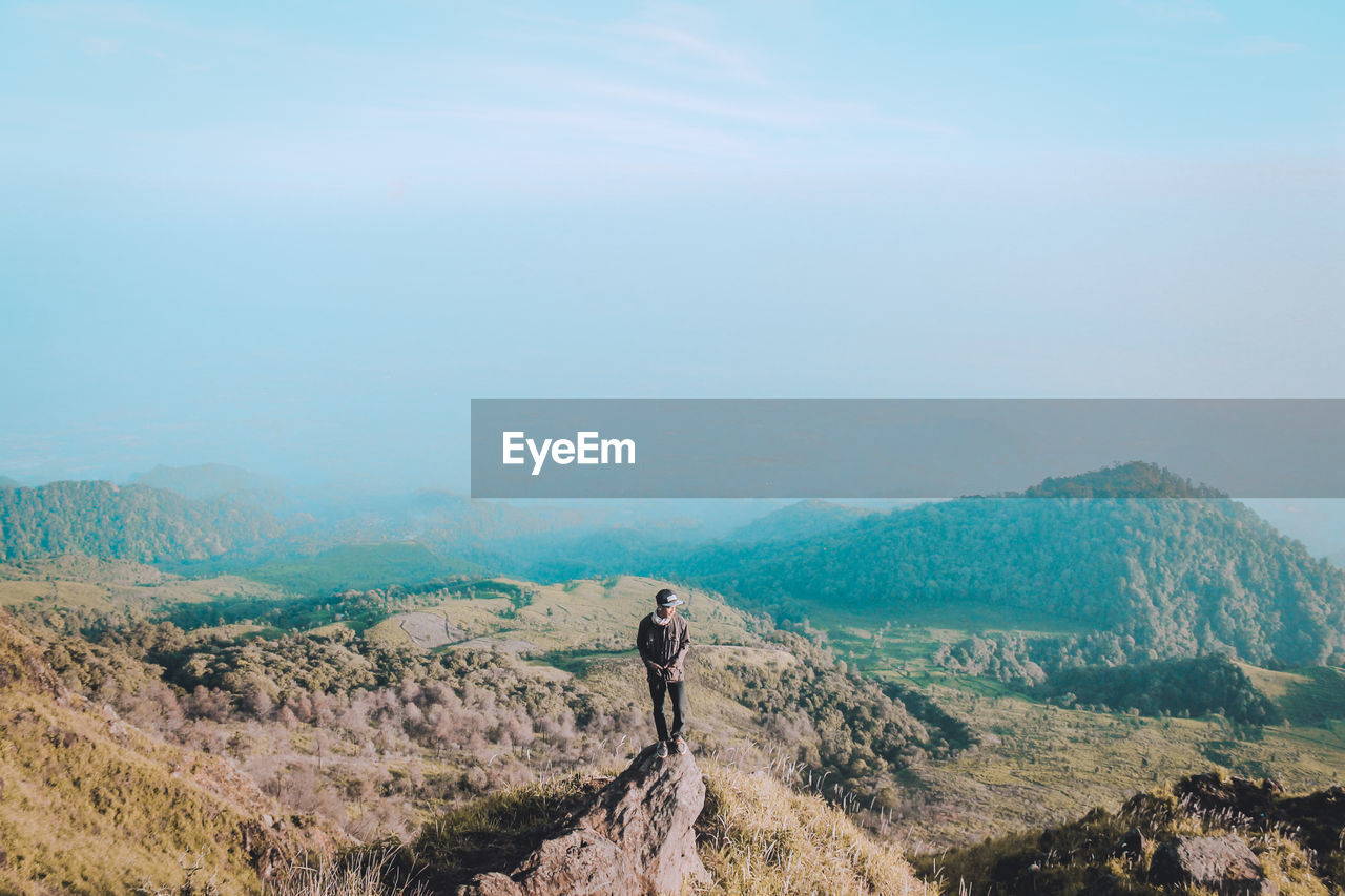 High angle view of young man standing on mountain against sky during sunny day