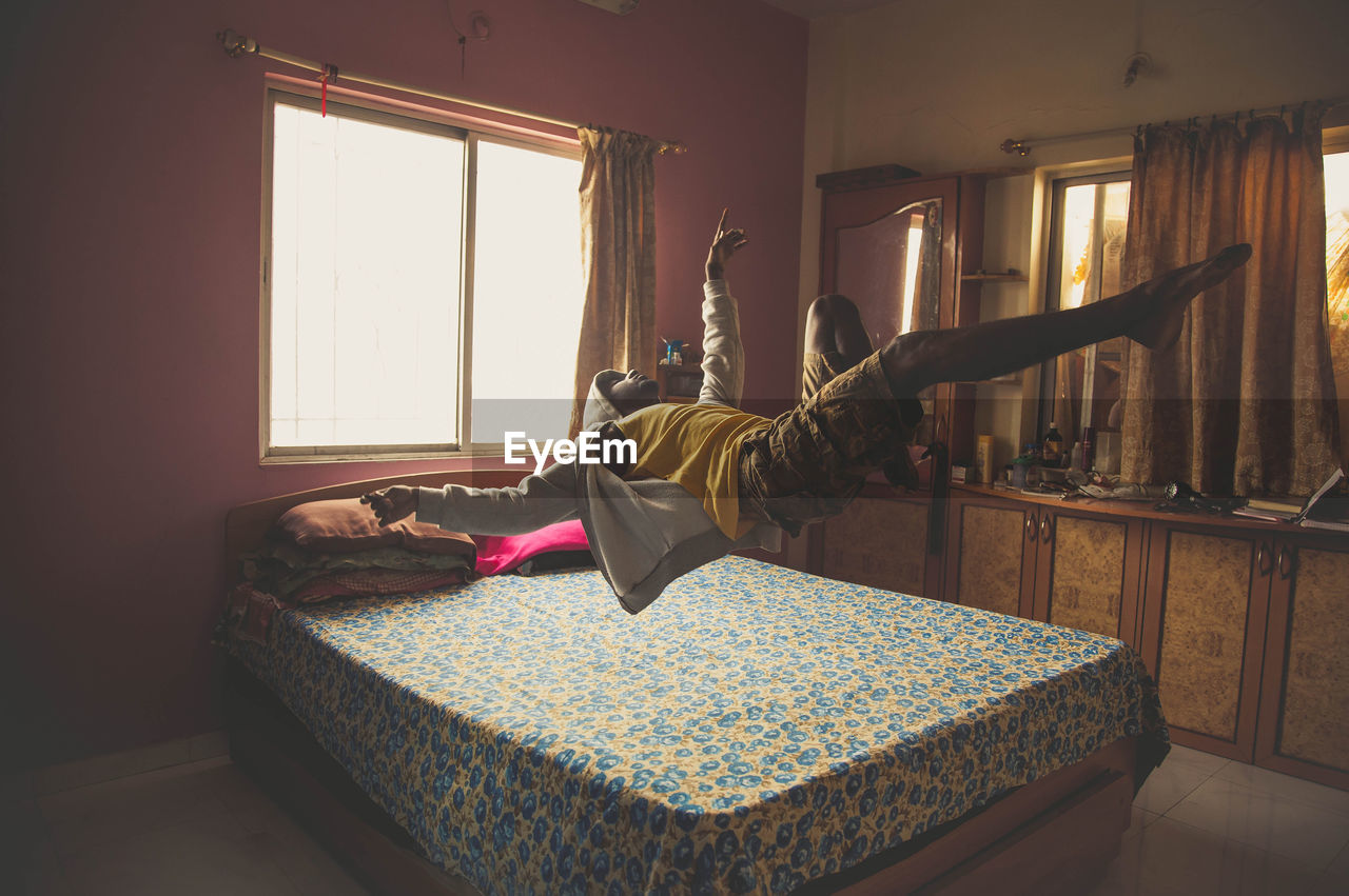 Full length of man levitating on bed at home