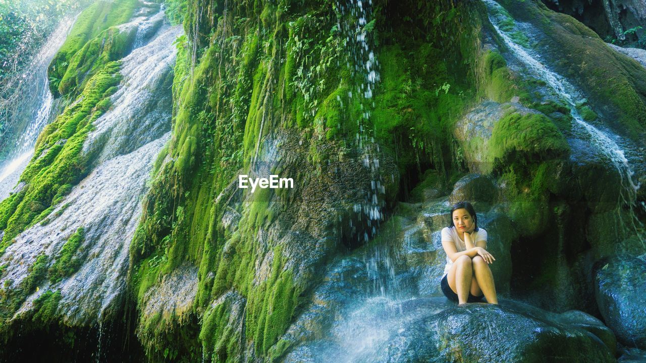 Portrait of woman sitting against waterfall in forest