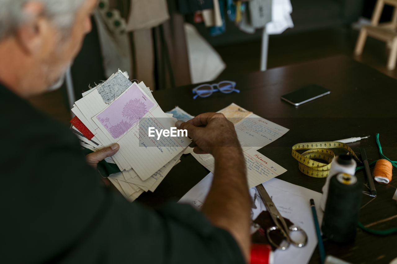 Mature male tailor looking at fabric swatch in work studio