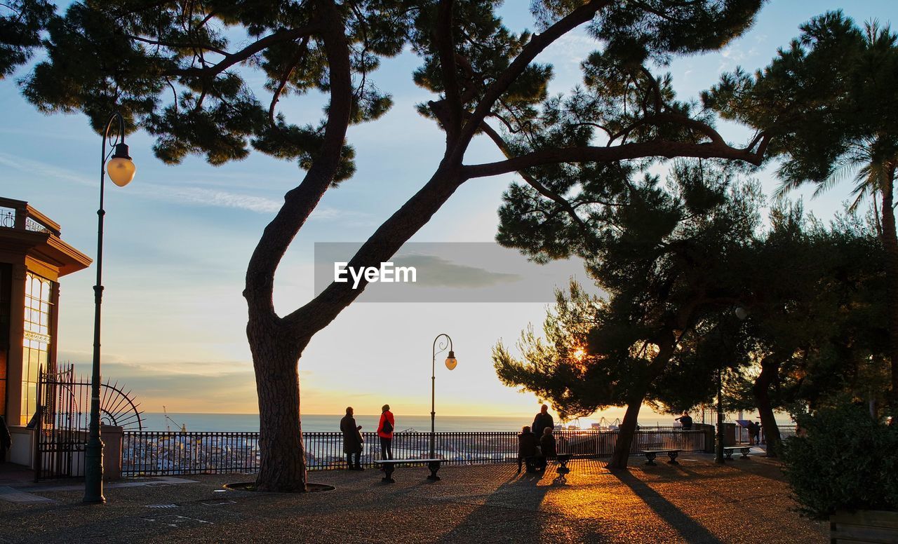 PEOPLE ON STREET BY SEA AGAINST SKY AT SUNSET