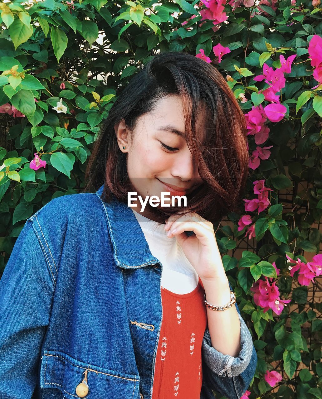 BEAUTIFUL YOUNG WOMAN LOOKING DOWN WHILE STANDING BY PLANTS