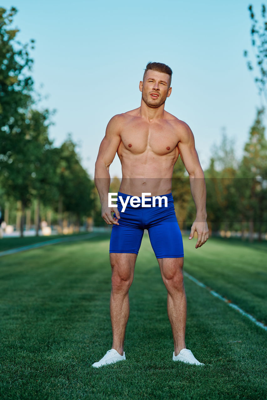 portrait of shirtless young man exercising on field