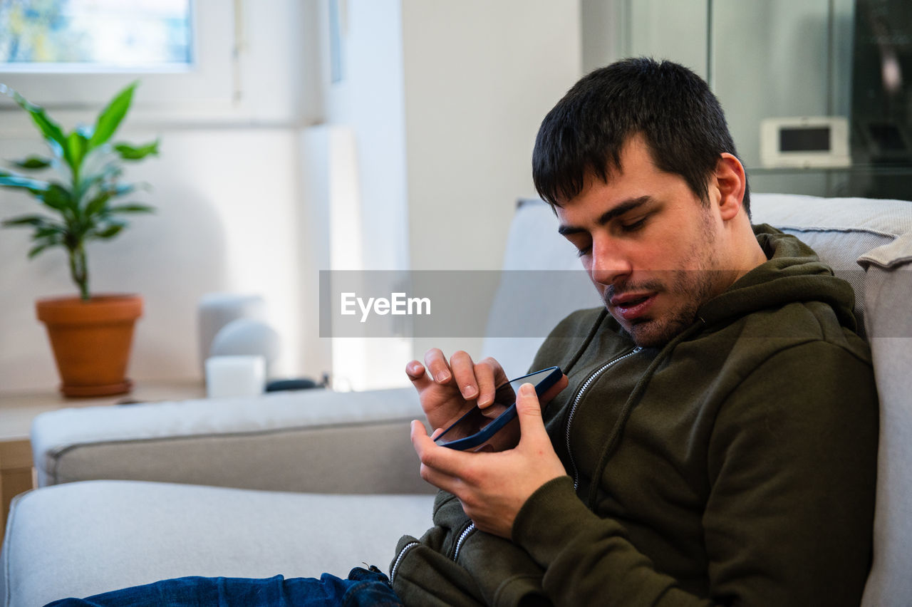 Male with eyesight disability scrolling mobile phone while sitting on couch at home