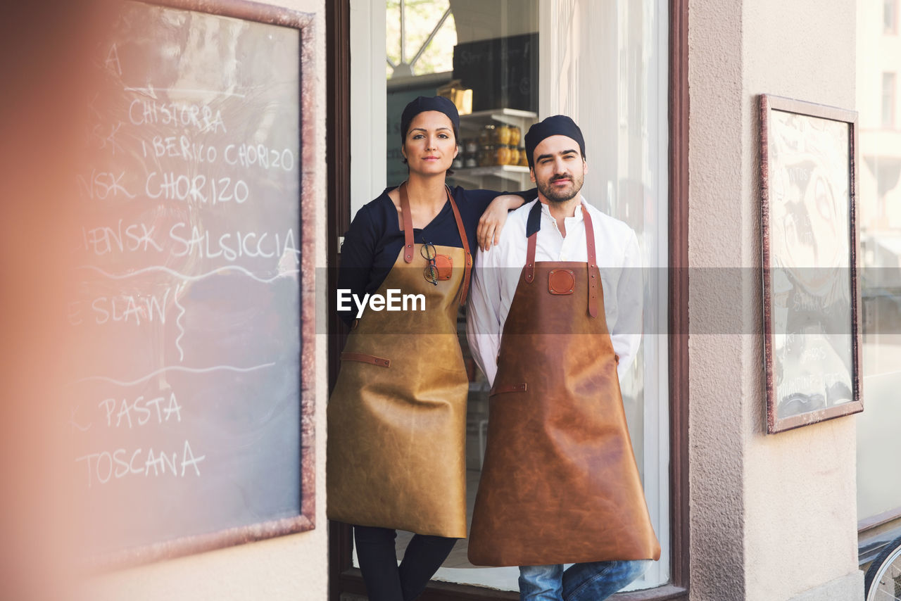 Portrait of confident male and female owners standing at grocery store entrance