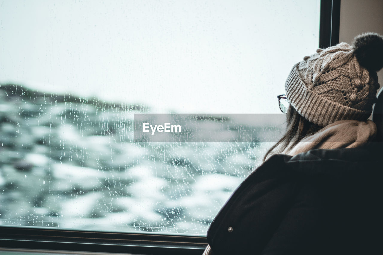 Woman looking through window during winter