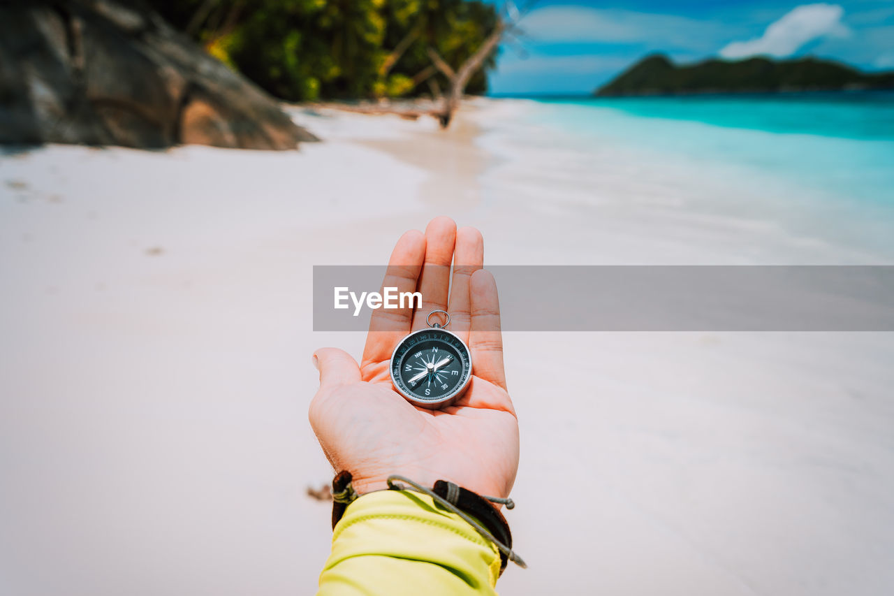 Close-up of hand holding navigational compass at beach