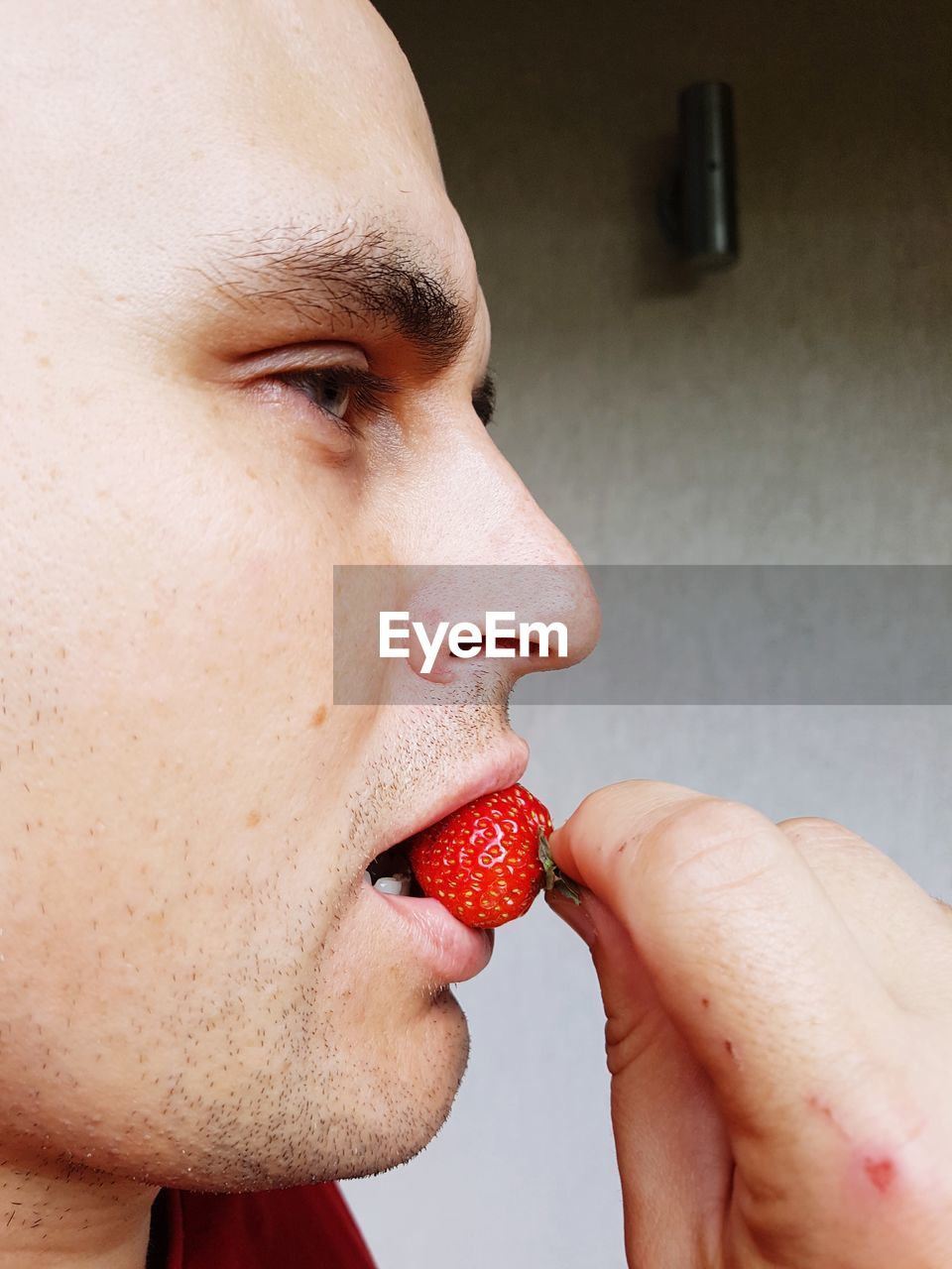 Side view of mid adult man eating strawberry against wall