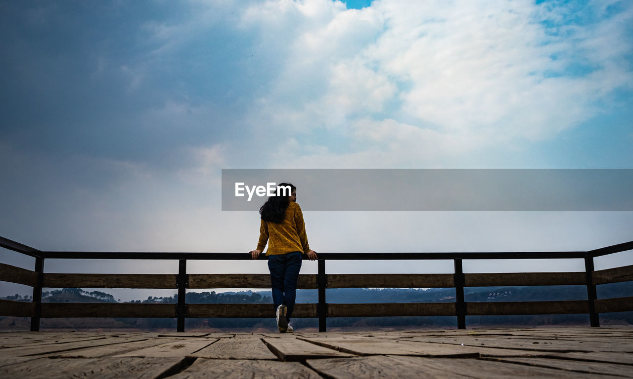 REAR VIEW OF WOMAN STANDING ON RAILING