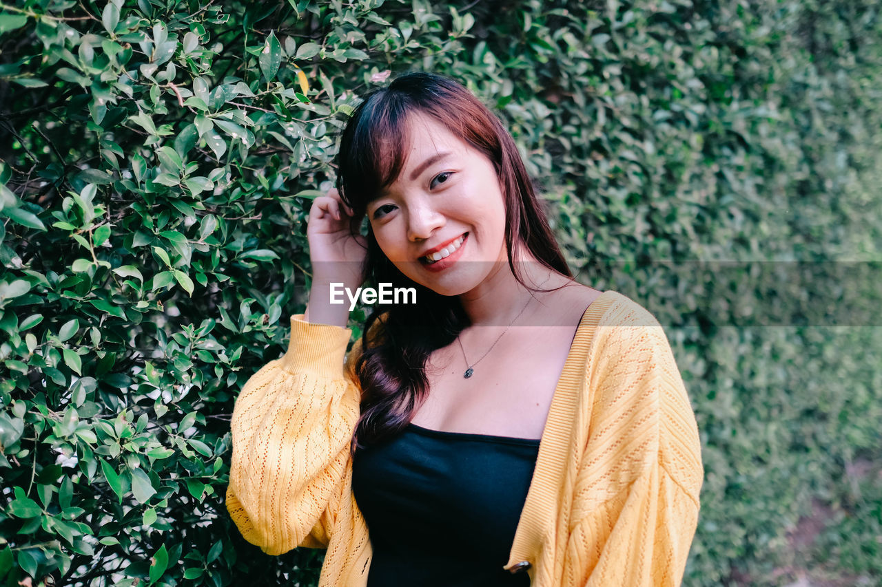 Close up of young pretty asian woman in blue yellow sweater with garden background.