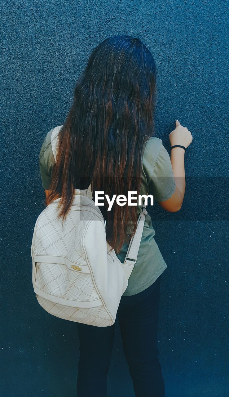 Rear view of woman with bag standing against wall