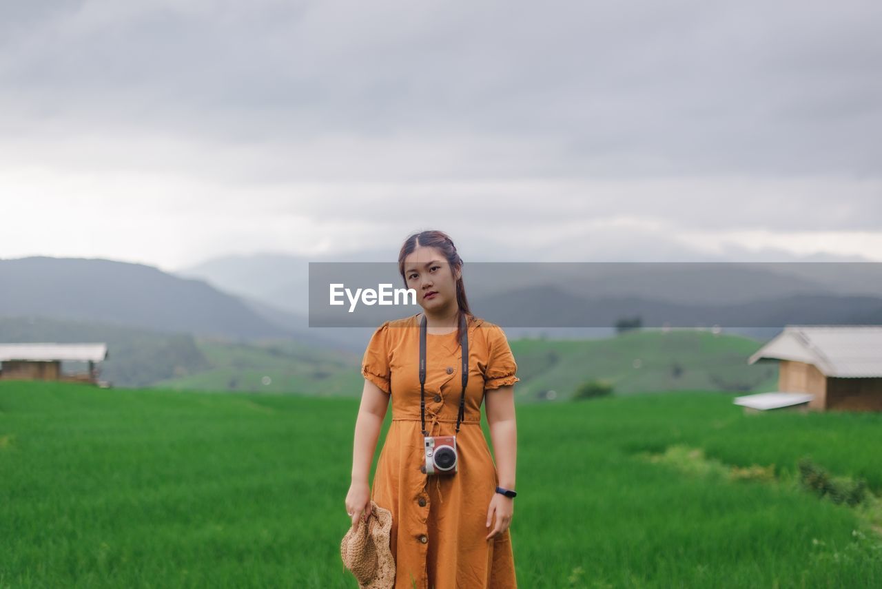 Portrait of young woman standing on landscape against sky