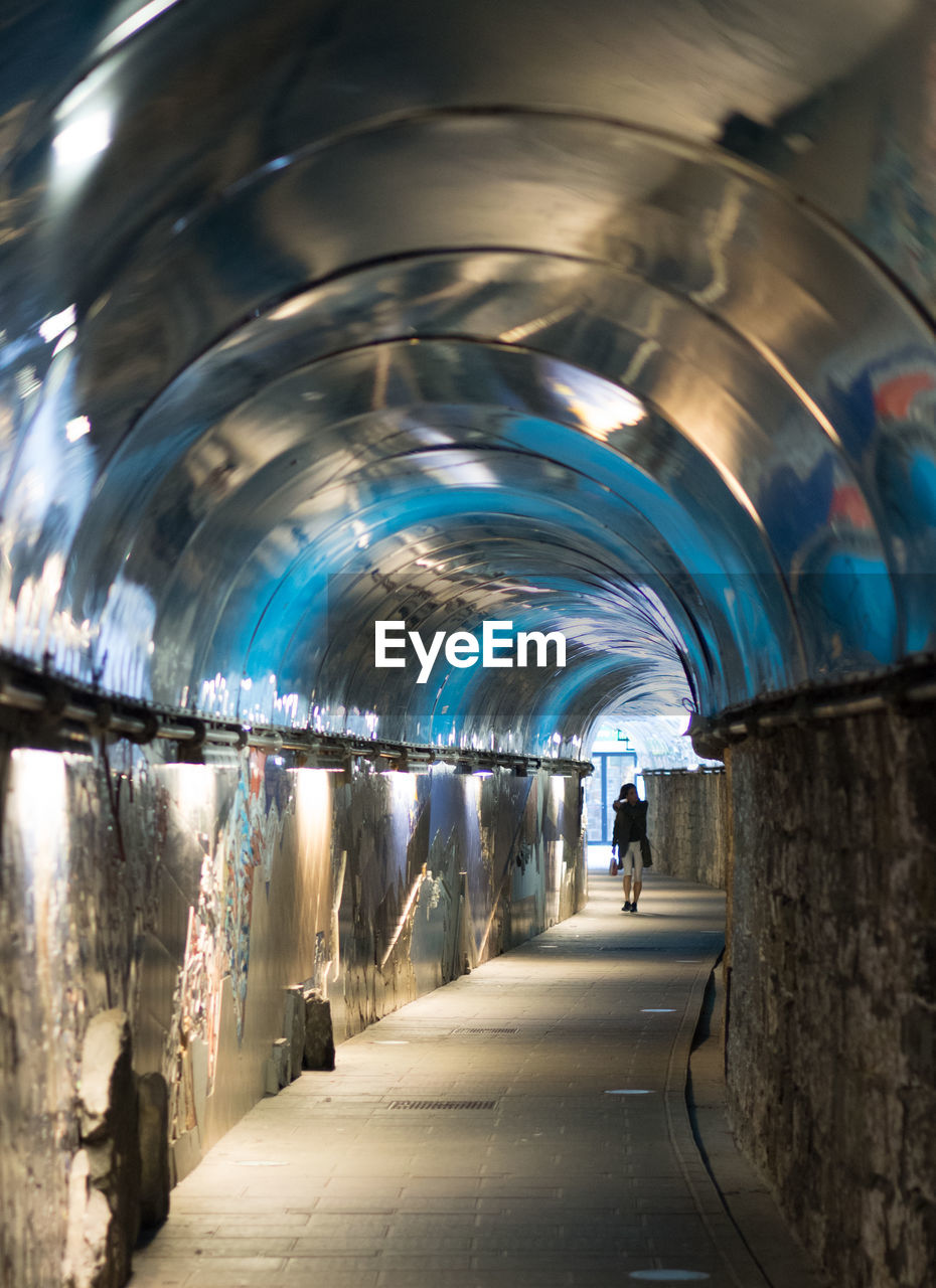 REAR VIEW OF MAN IN ILLUMINATED UNDERGROUND WALKWAY