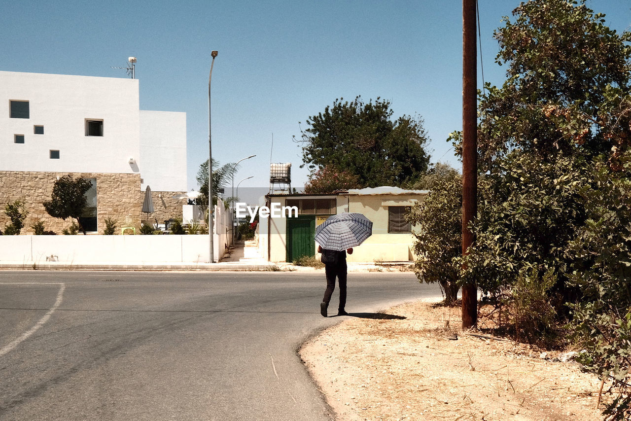 View of man walking on road, using his umbrella against sun
